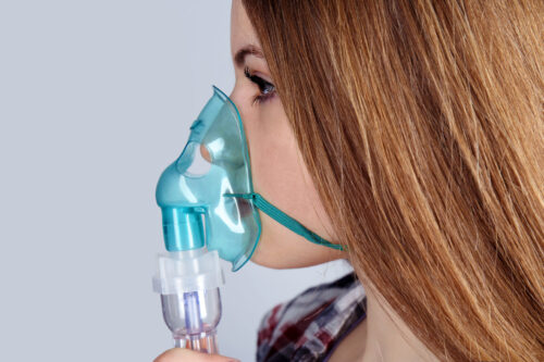 Young Woman Using Nebulizer For Asthma And Respiratory Diseases On Light Background