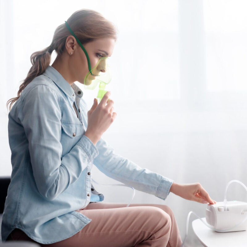 Side View Of Woman In Respiratory Mask Touching Compressor Inhaler